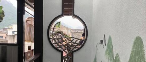 A circular decorative element with a geometric pattern, a view of buildings through a window, and a wall with green abstract designs.
