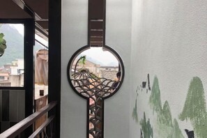 A circular decorative element with a geometric pattern, a view of buildings through a window, and a wall with green abstract designs. - Pailou Guesthouse (Yueqing)