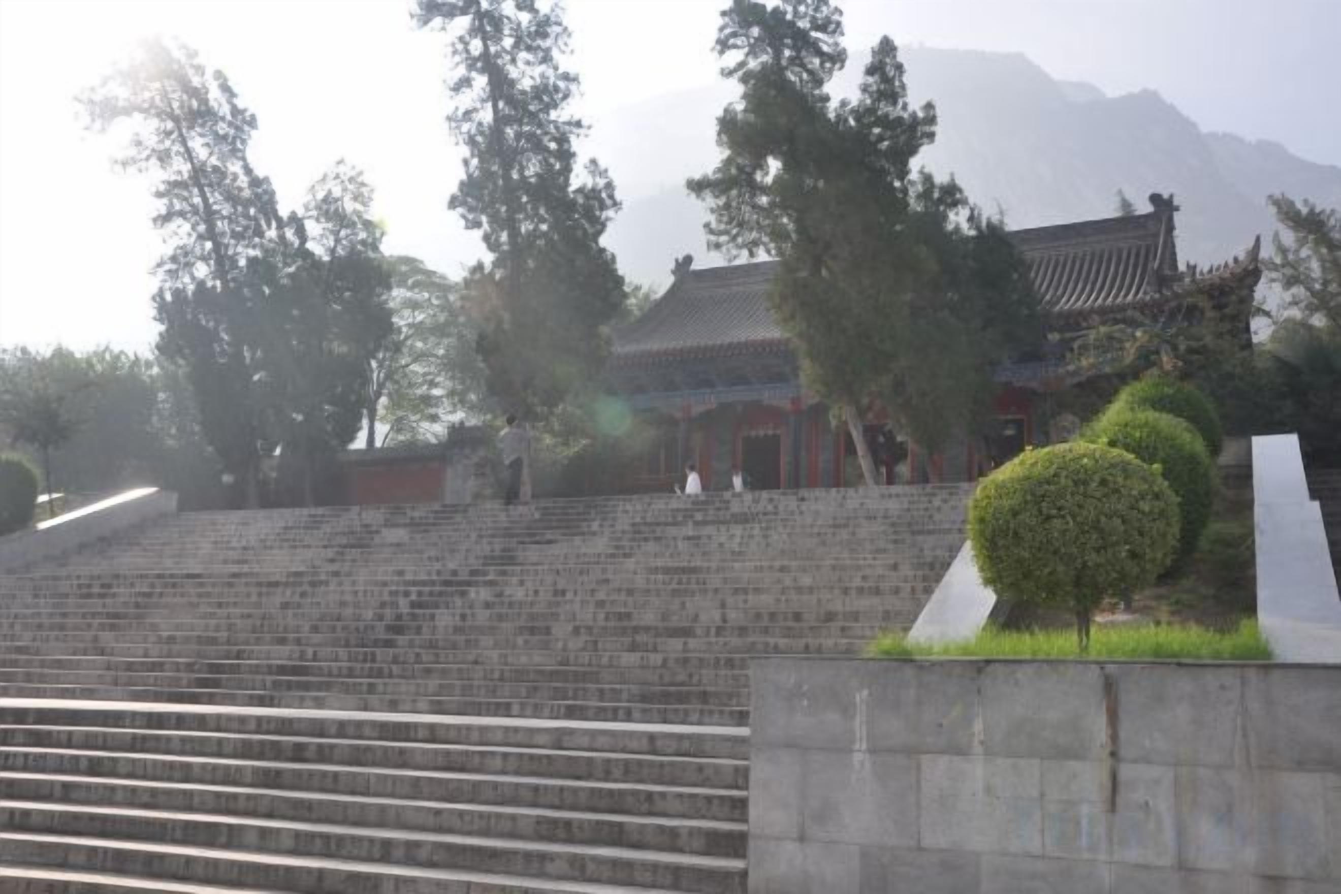 A traditional building with a tiled roof, surrounded by trees and a stone staircase leading up to it.