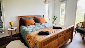 Ein geräumiges Schlafzimmer mit einem großen Holzbett, einer Hängelampe und großen Fenstern, die für natürliches Licht sorgen.