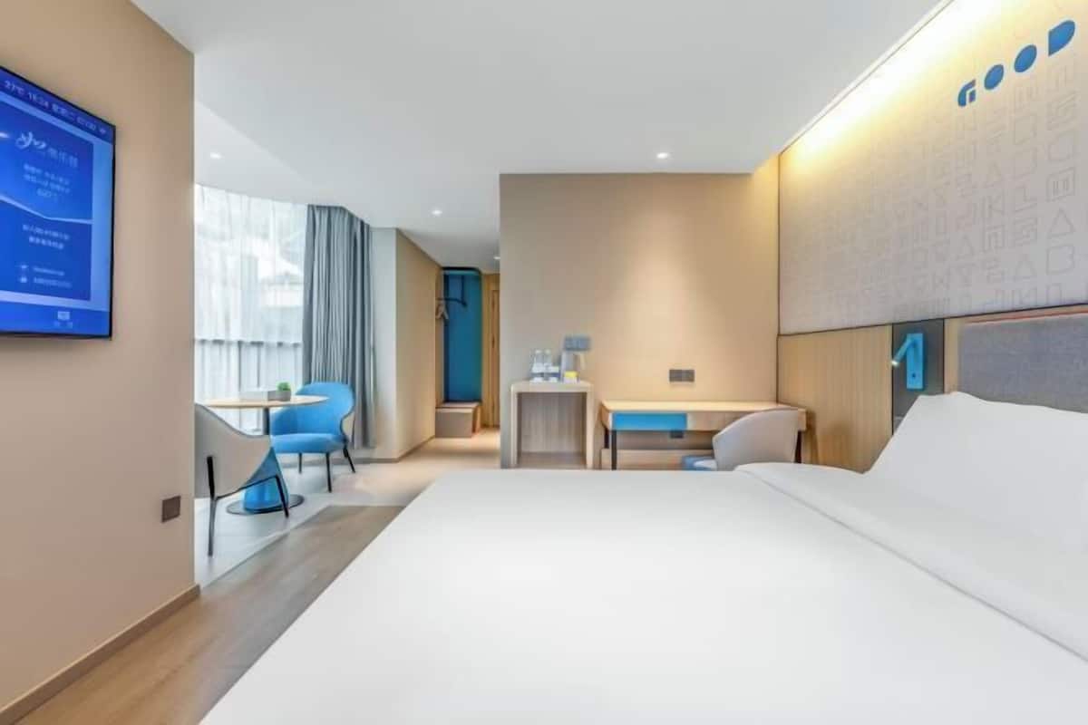 A hotel room with a bed, a desk, a chair, a TV, and a window.
