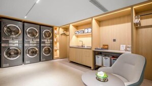 A modern laundry room with three washing machines, a sink, and a seating area with a table. - Homeinn · neo (Liuzhou Five Star Pedestrian Street) (Liuzhou)