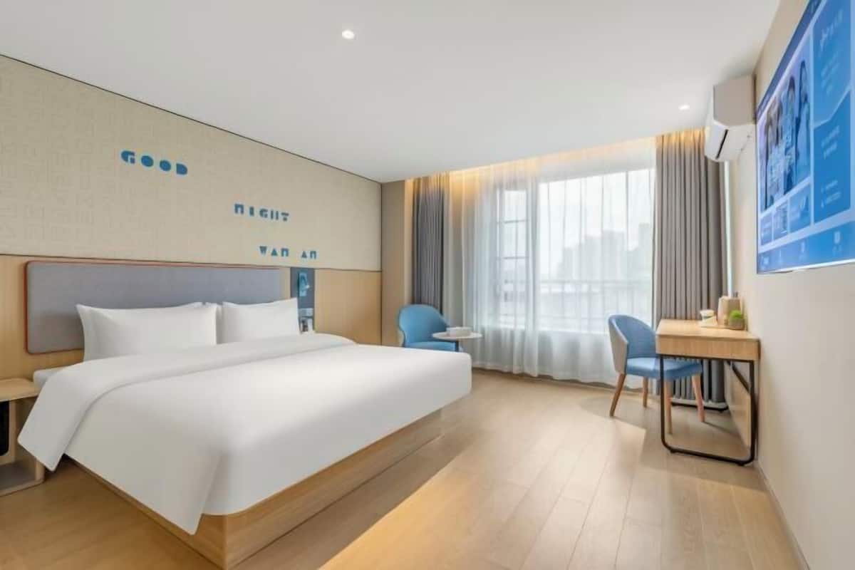 A hotel room with a large bed, a desk, a chair, and a window with curtains.