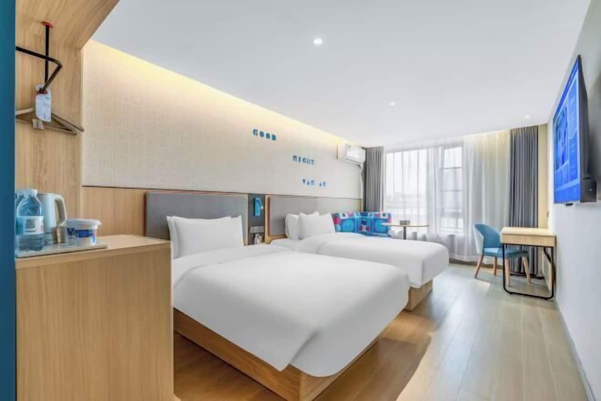 A hotel room with two beds, a desk, a TV, and a window.