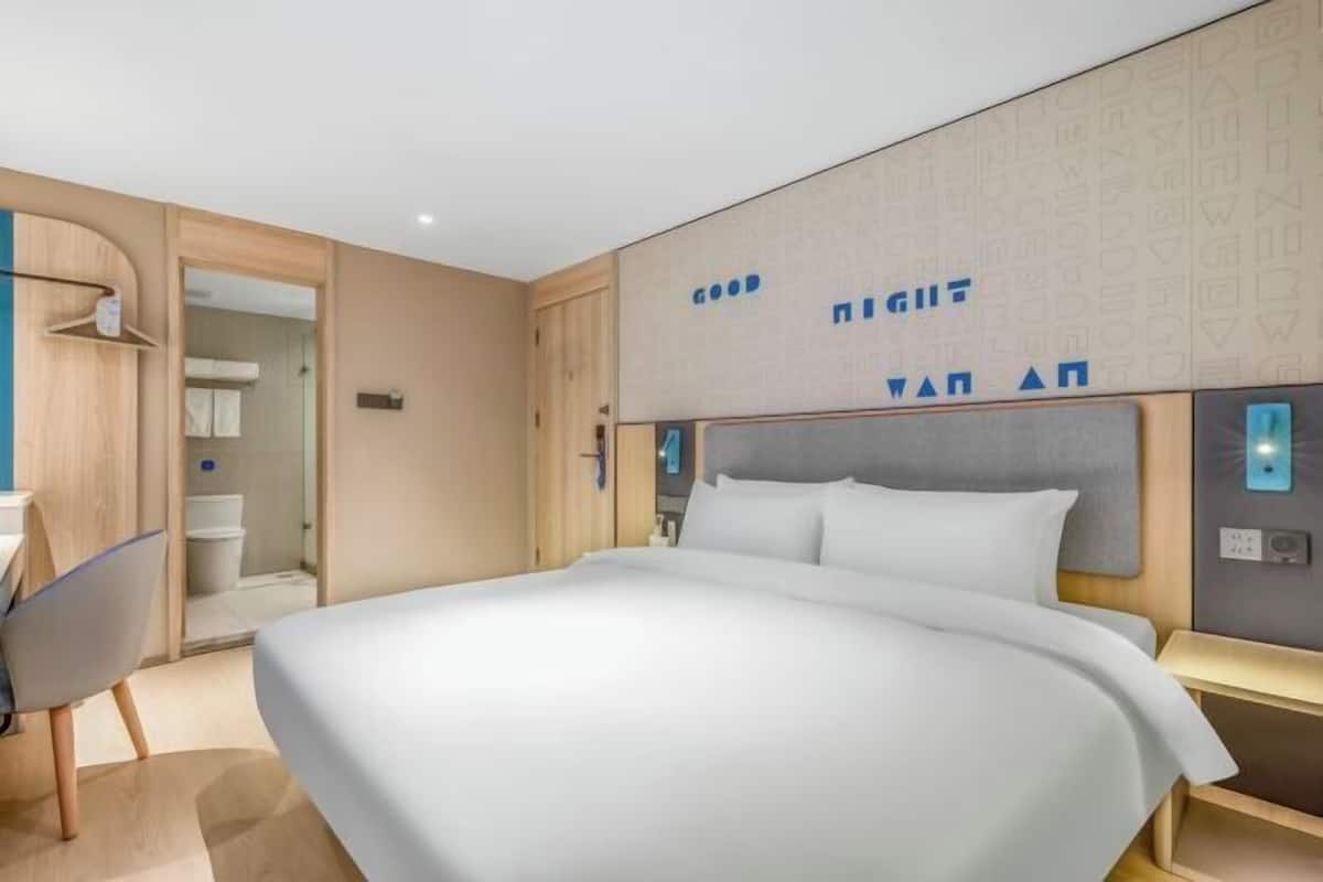 A modern hotel room with a large bed, a desk, and a shower area.