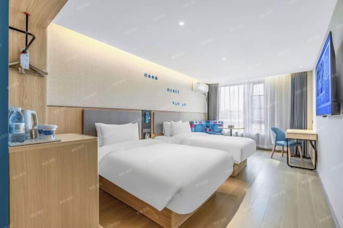 A hotel room with two beds, a desk, a chair, a TV, and a window with curtains.