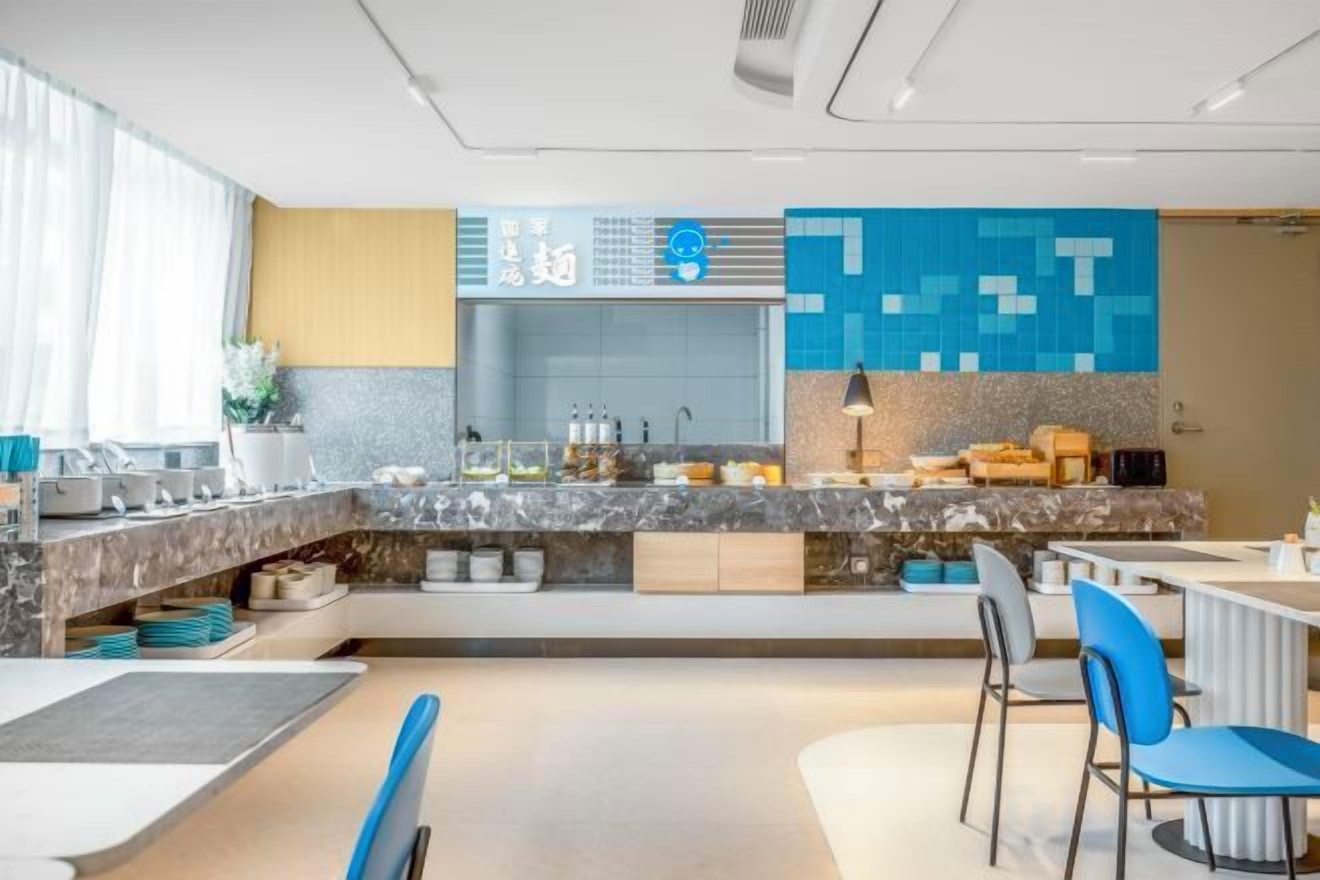 A modern kitchen with a marble countertop, built-in appliances, and a seating area with blue chairs.