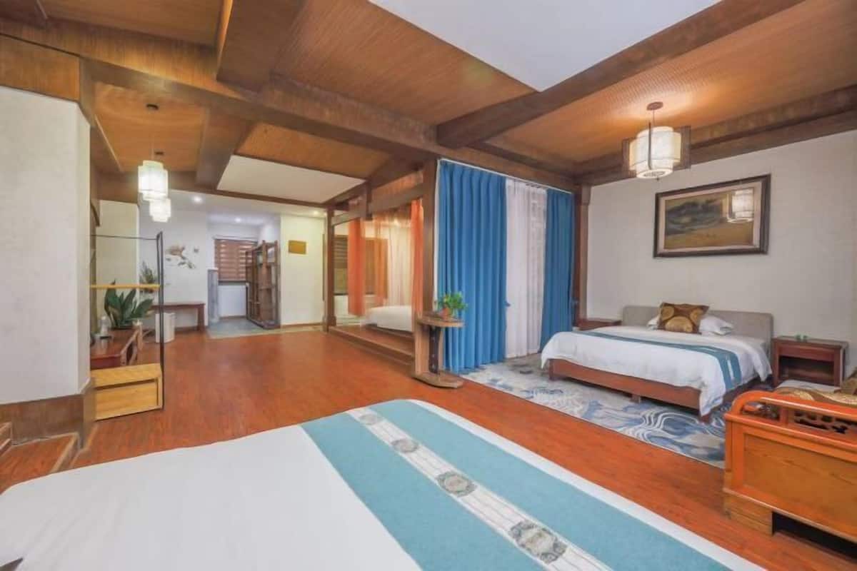 A hotel room with a wooden ceiling, a bed with a blue and white bedspread, a bedside table, a nightstand, a wall-mounted lamp, and a painting.