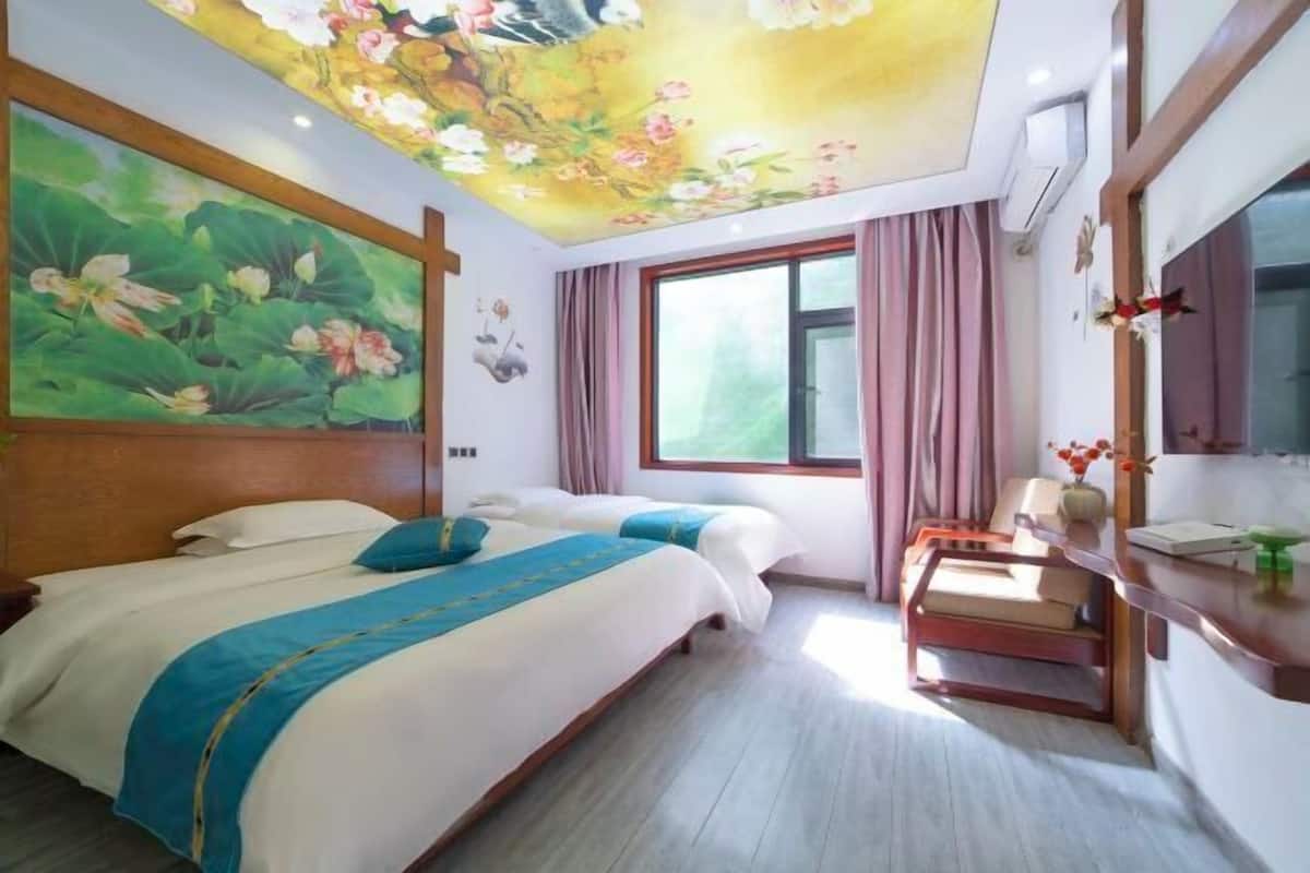 A hotel room with two beds, a desk, a large window, and a ceiling mural.