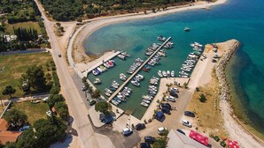 An aerial view of a marina with boats docked, a sandy beach, and surrounding greenery.