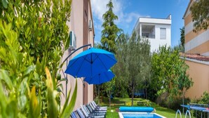 A swimming pool with lounge chairs and a blue umbrella, surrounded by well-maintained grass and trees.