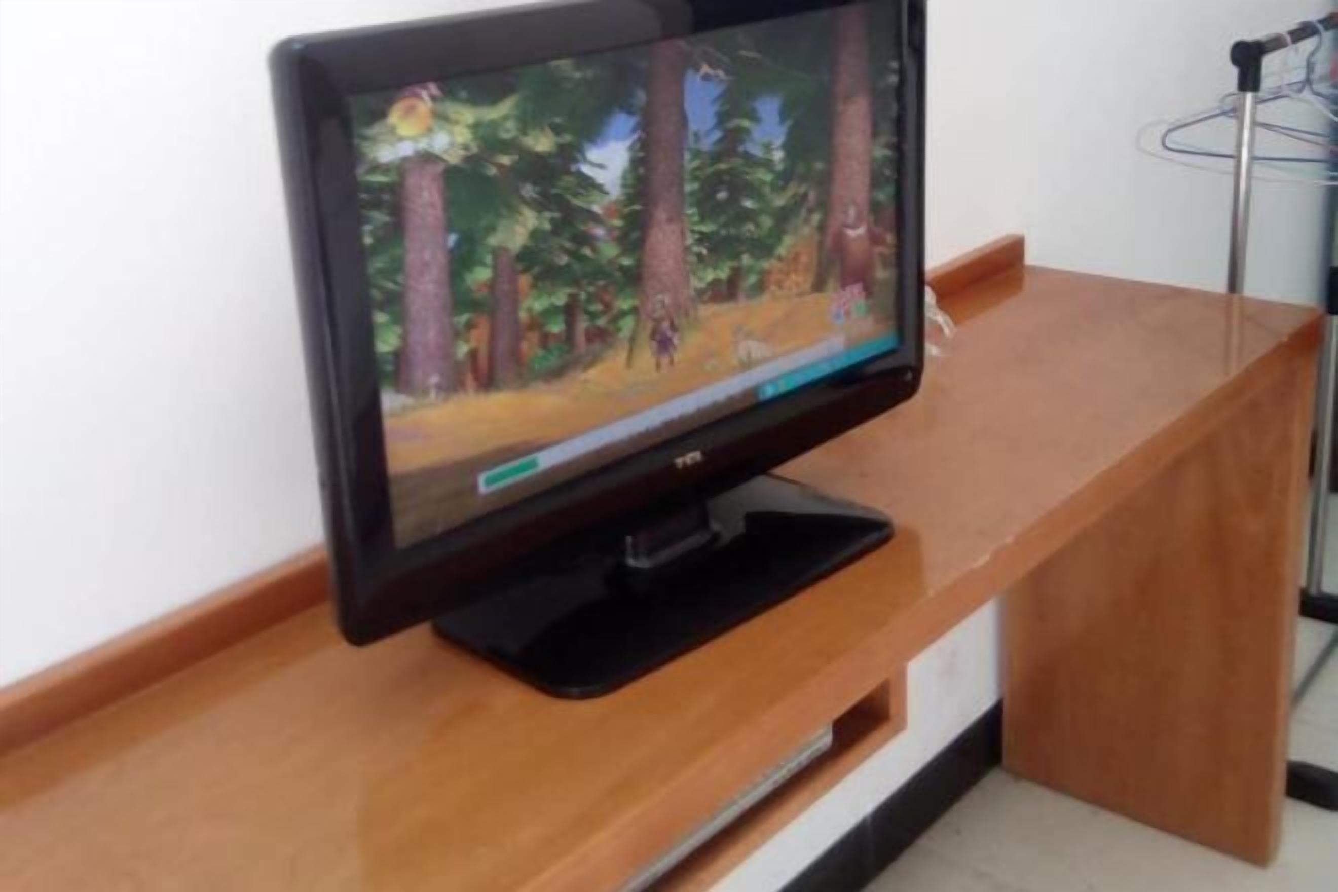 A flat-screen TV on a wooden stand in a room with a white wall and a metal hanger in the background.