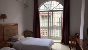A hotel room with two beds, a wooden headboard, a desk with a chair, a TV, and a large window with curtains.