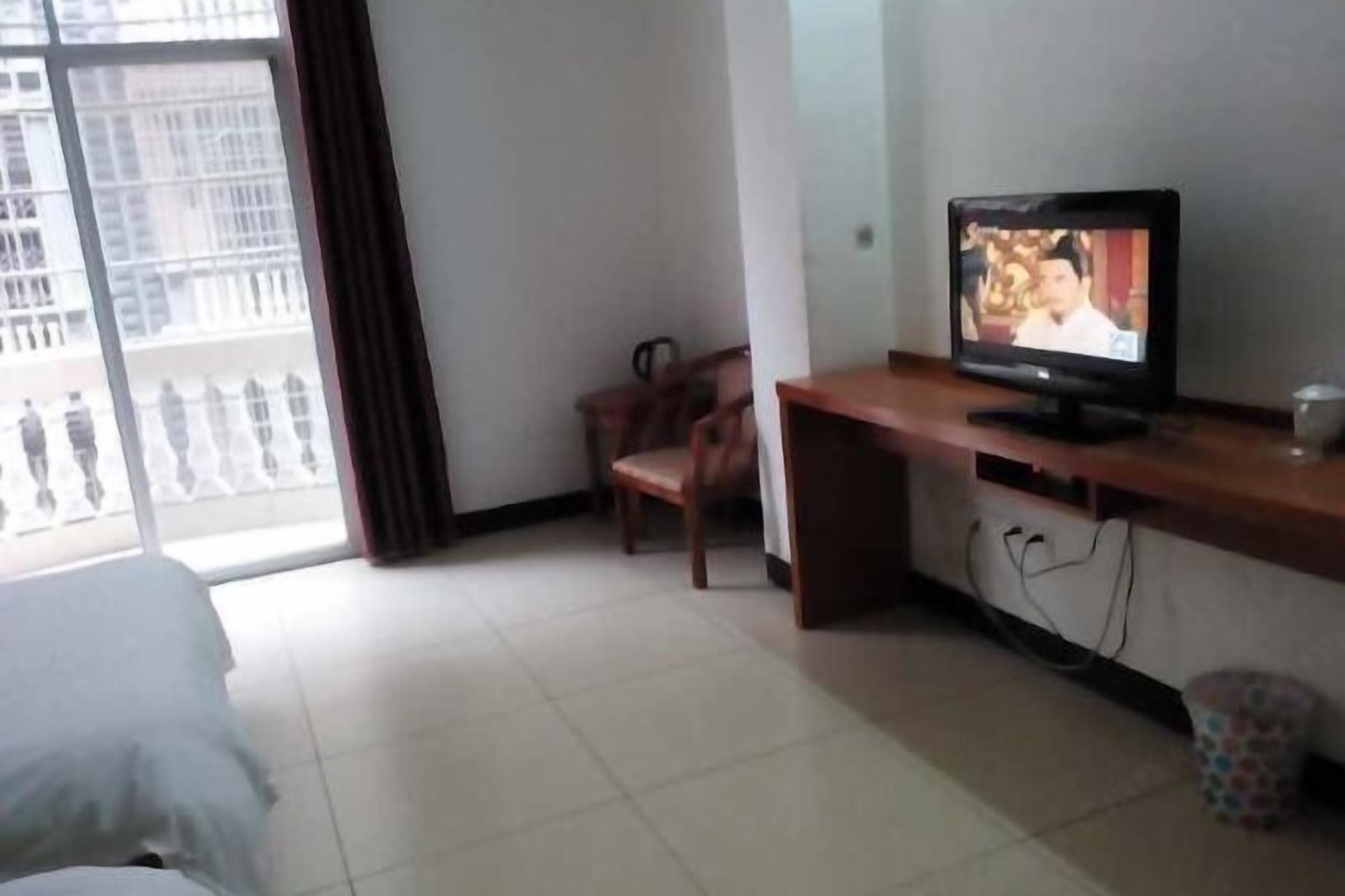 Habitación de hotel con cama, televisión sobre un escritorio de madera, una silla y vista a un edificio a través de una ventana.