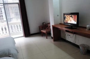 Quarto de hotel com uma cama, uma televisão sobre uma escrivaninha de madeira, uma cadeira e vista para um edifício pela janela.