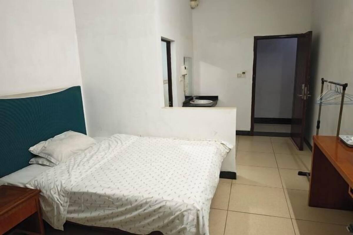 A room with a bed, a desk, a wardrobe, and a door leading to another room.
