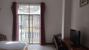 A hotel room with a bed, a desk with a computer, and a balcony with a view of buildings.