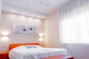 A bedroom with a bed, a nightstand, a wall-mounted light, and a window with curtains. - Apartments Mala Vila Joy - Two Bedroom Apartment with Balcony and Sea View (Rab)