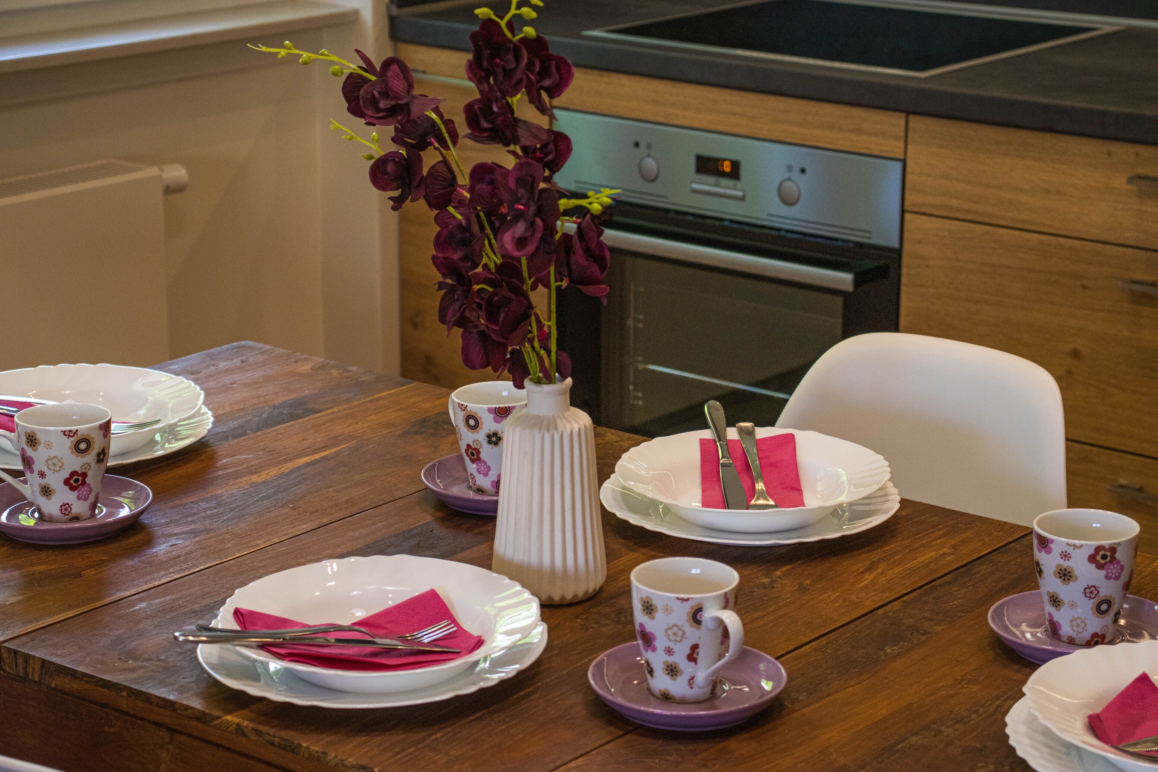 Une table à manger dressée avec des assiettes, des tasses et un vase rempli de fleurs.