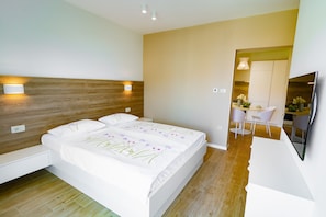 Un dormitorio moderno con cabecera de madera, una cama grande con ropa de cama floral, una mesita de noche y un televisor montado en la pared.