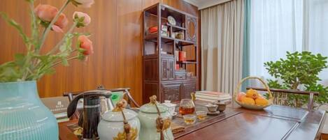 A dining table with tea sets, a vase with flowers, a bookshelf, and a window with curtains.