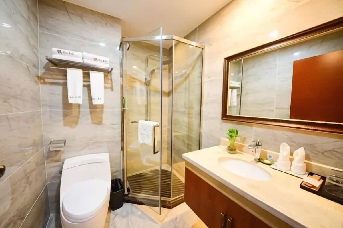 Une salle de bain moderne avec une douche à parois de verre, des toilettes blanches, un mur recouvert de carreaux de marbre et un grand miroir.