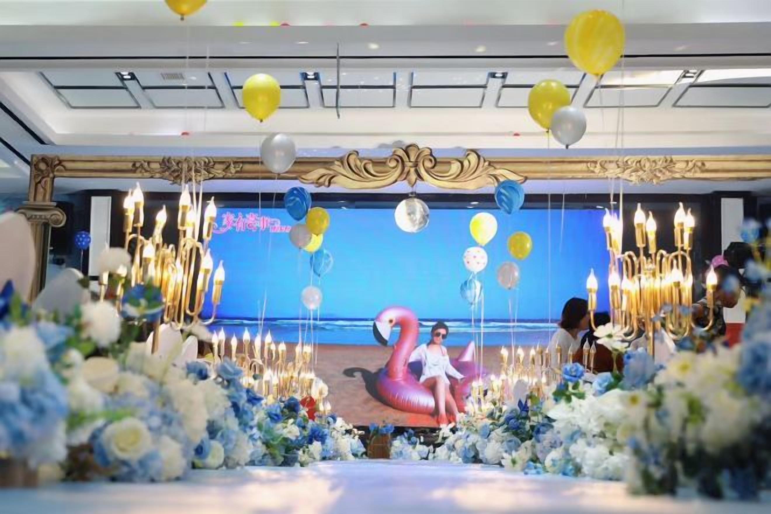 Un espacio decorado para un evento, con escenario, arreglos florales y globos.