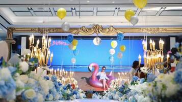 Un espacio decorado para un evento, con escenario, arreglos florales y globos.
