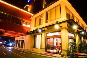 A two-story hotel with a covered entrance, large windows, and potted plants.