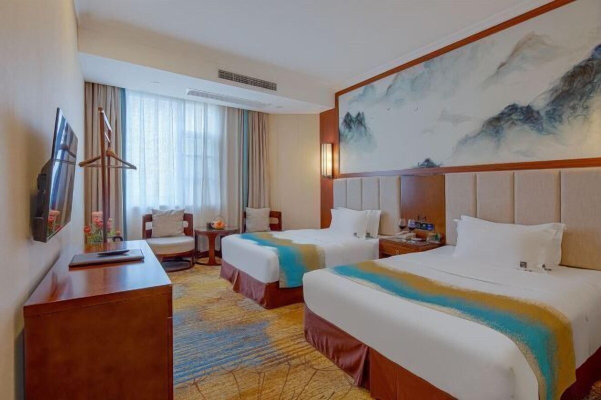 Habitación de hotel con dos camas, un escritorio, una silla, un televisor y un cuadro en la pared.