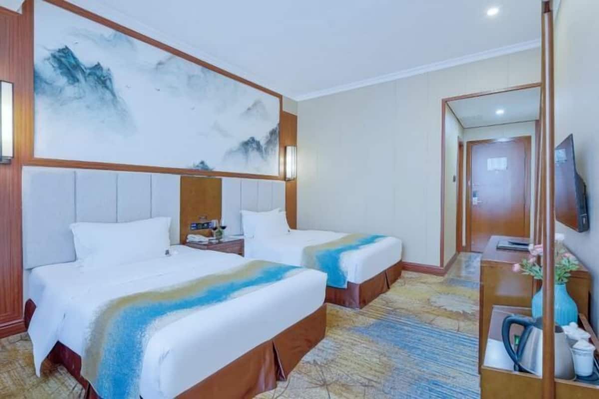 Une chambre d’hôtel avec deux lits, un grand tableau au mur, un bureau avec une chaise et une télévision.