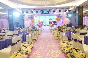 A banquet hall with tables arranged for an event, a stage at the front, and floral decorations along the aisle. - Hengshan Hotel (Hengshan County)