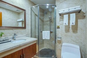 Un baño con ducha de vidrio, lavamanos, inodoro y toallero con toallas.