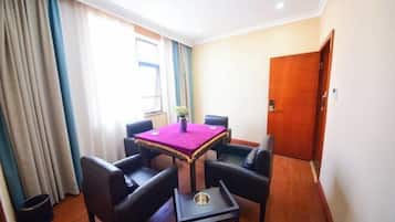 A room with a table, four chairs, a small side table, a door, and a window with curtains.