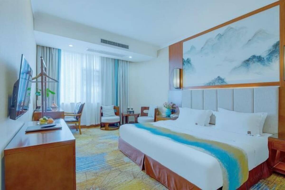 Une chambre d’hôtel avec un lit, un bureau, une chaise, une télévision et un tableau au mur.