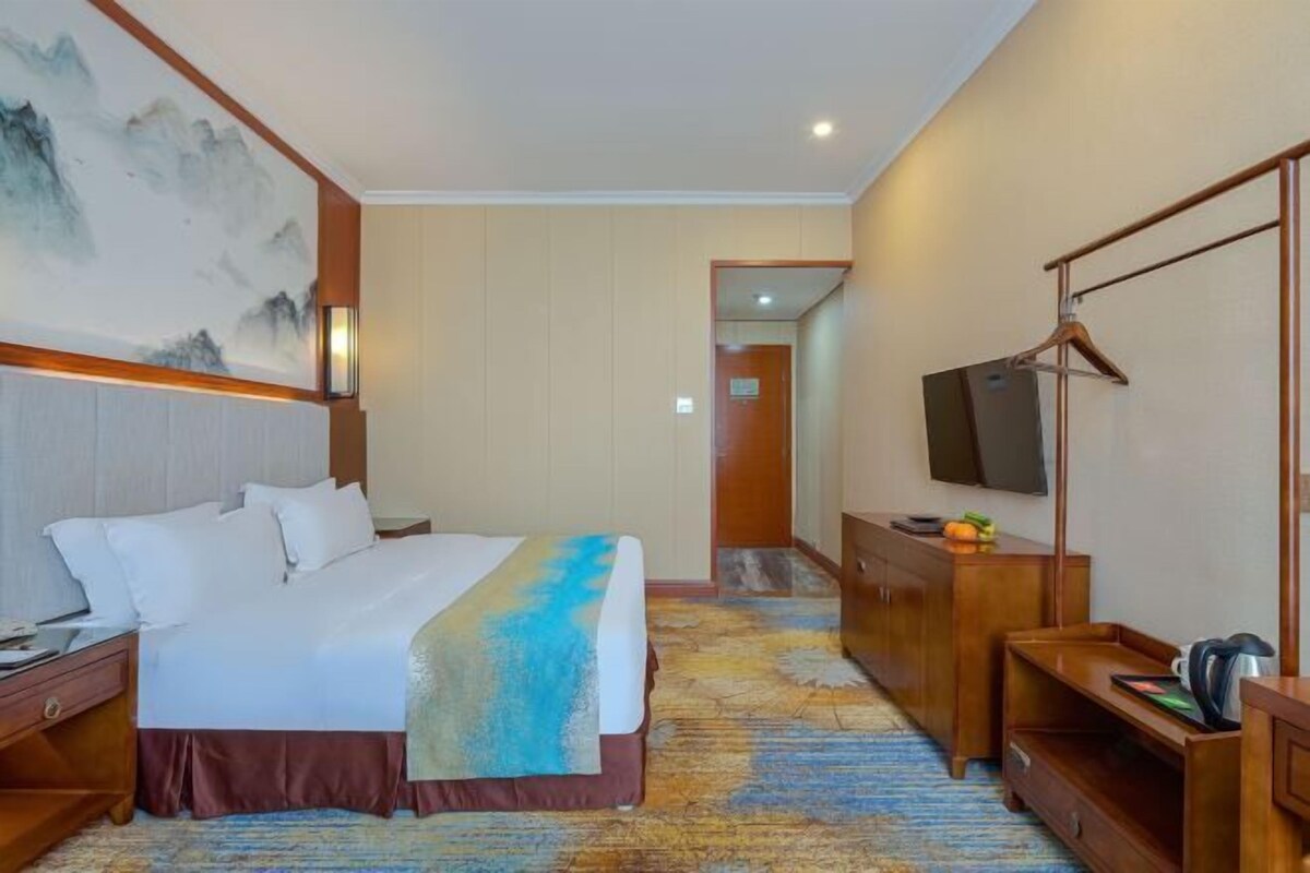 Habitación de hotel con cama, televisor, escritorio, cómoda y un cuadro en la pared.