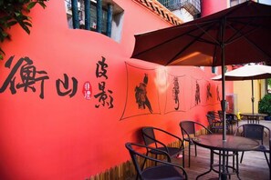 An outdoor seating area with tables and chairs, a red wall with black calligraphy, and a large umbrella providing shade. - Hengshan Hotel (Hengshan County)