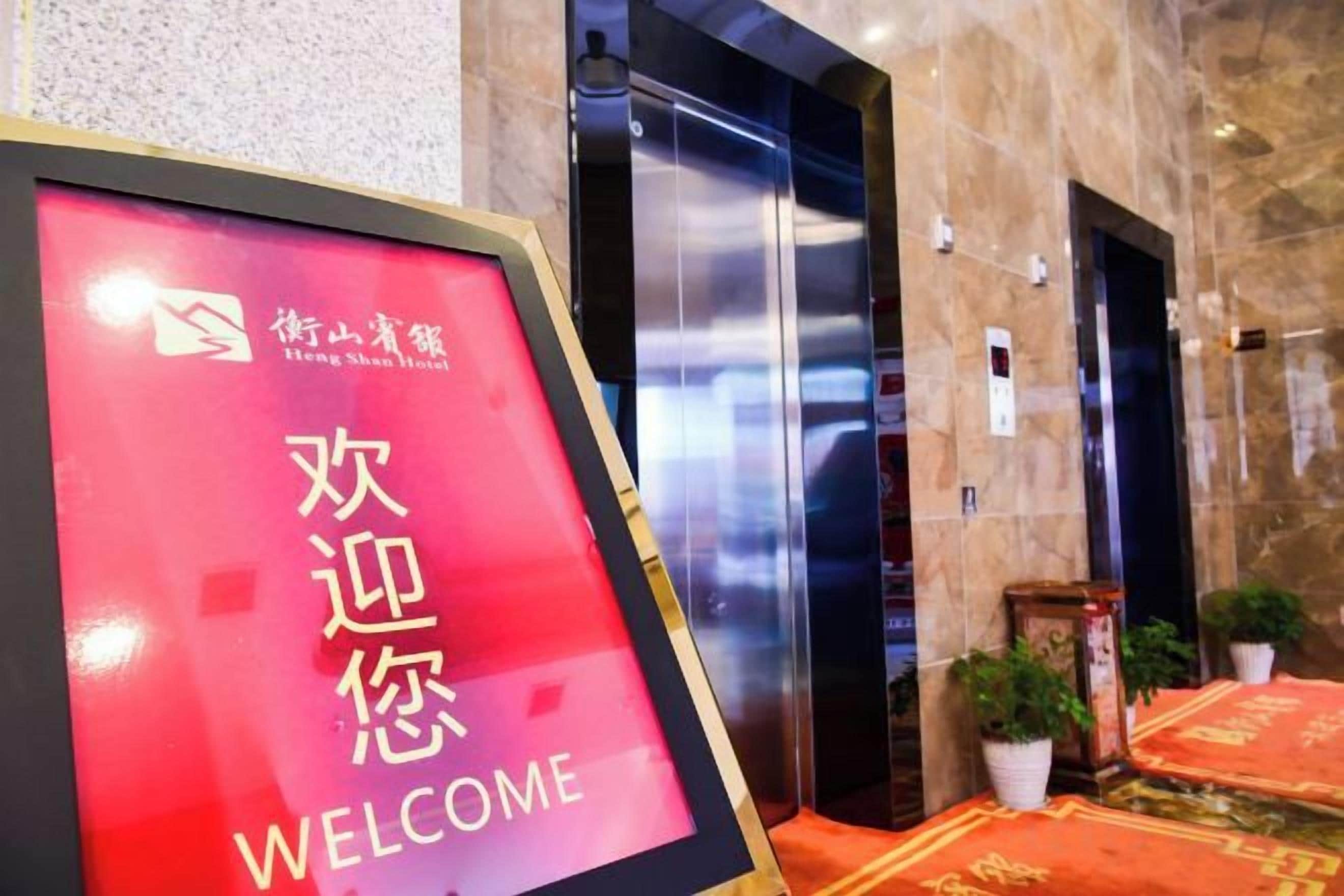 A hotel reception area with a welcome sign, elevators, and potted plants.