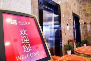 A hotel reception area with a welcome sign, elevators, and potted plants. - Hengshan Hotel (Hengshan County)