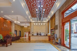 A hotel lobby with a reception desk, chandeliers, and a large window.