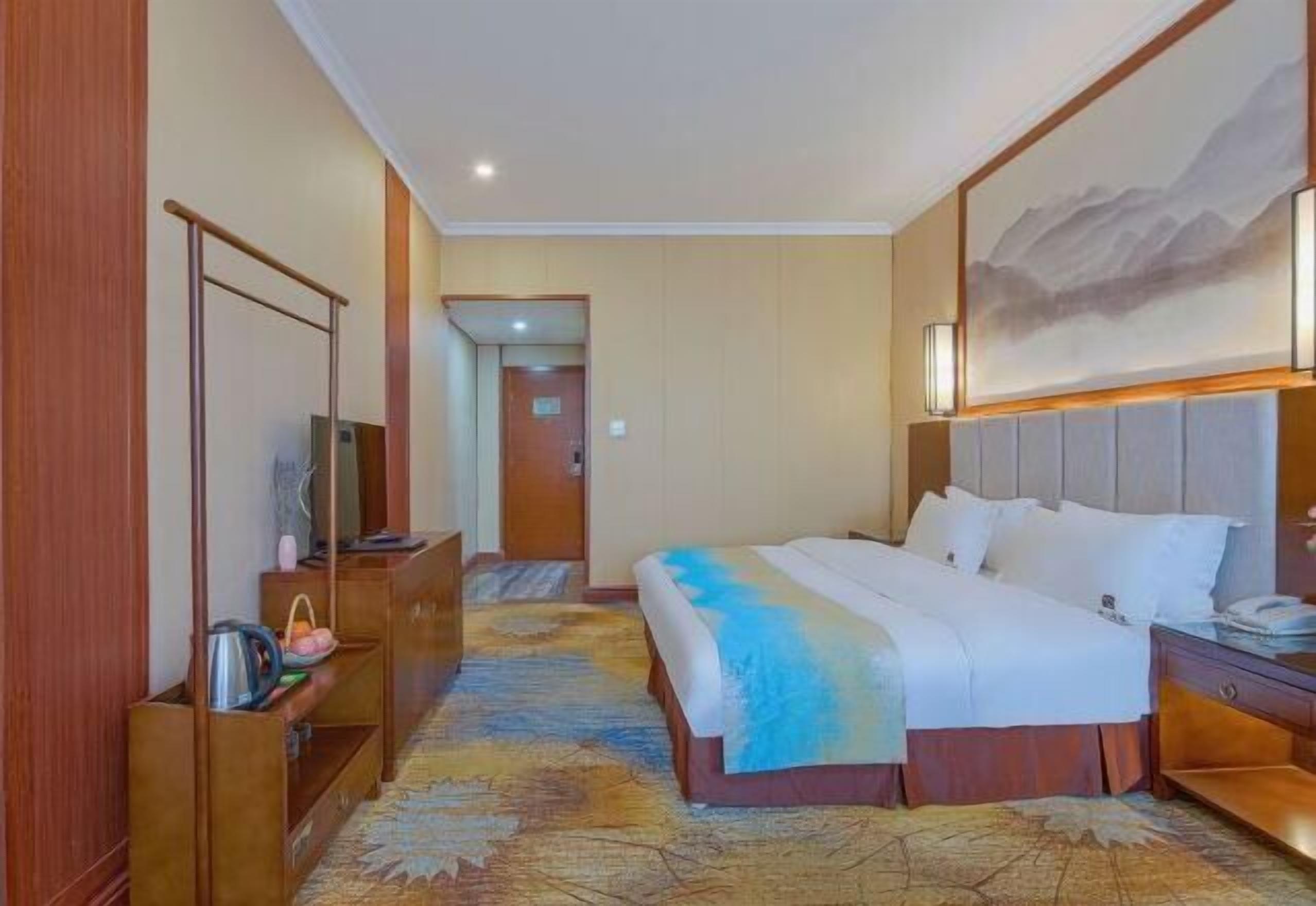 Habitación de hotel con cama, escritorio, silla, televisor y un cuadro en la pared.