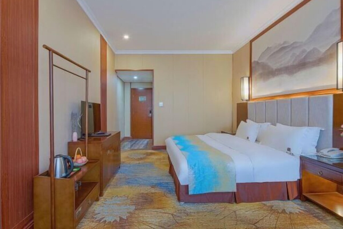 Habitación de hotel con cama, escritorio, silla, televisor y un cuadro en la pared.