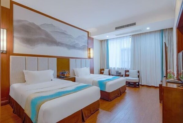 Habitación de hotel con dos camas, un cuadro grande en la pared, un escritorio con una silla y una ventana con cortinas.