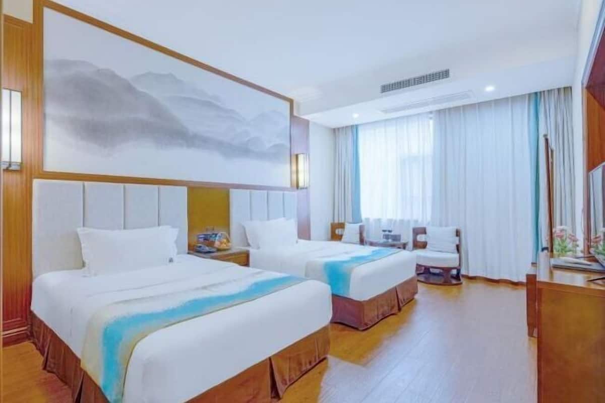 Une chambre d’hôtel avec deux lits, un grand tableau, une fenêtre avec des rideaux et un plancher en bois.