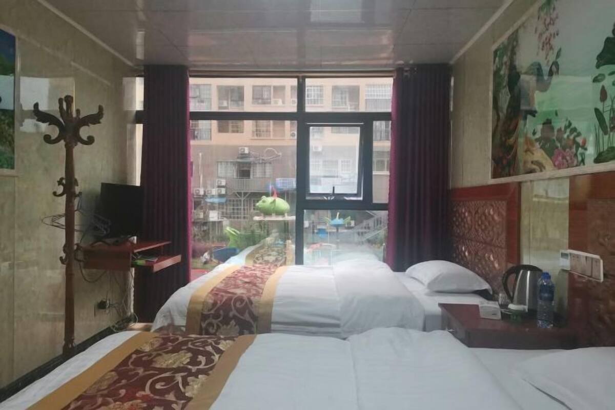 Habitación de hotel con dos camas, un escritorio con silla, televisor y ventana con cortinas.