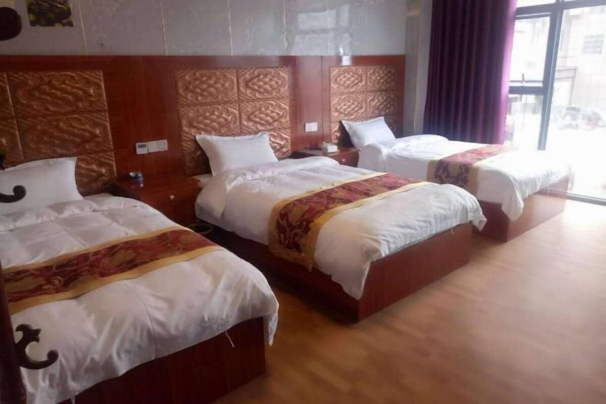 Una habitación de hotel con tres camas, cada una con cabecera de madera y ropa de cama blanca.