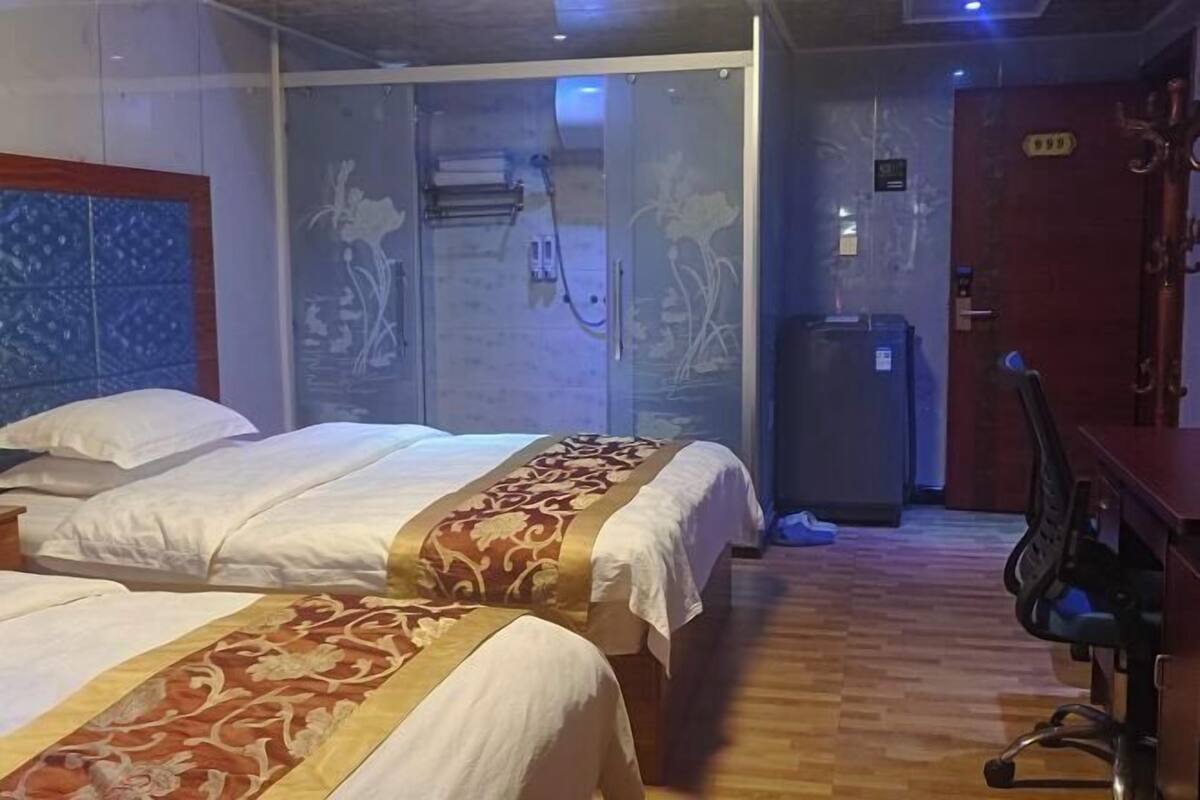 Habitación de hotel con dos camas, zona de ducha, escritorio y una puerta con un número.