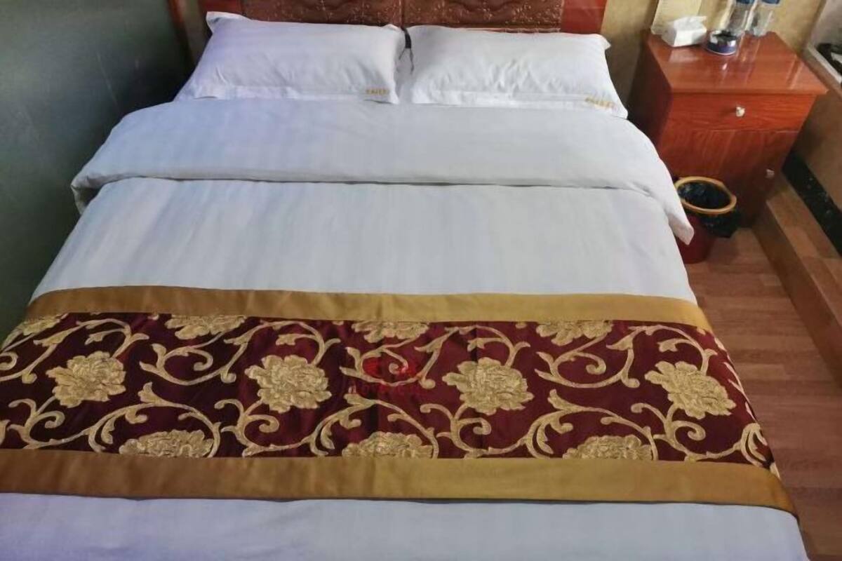 Una cama con ropa de cama blanca y una manta decorativa roja y dorada.