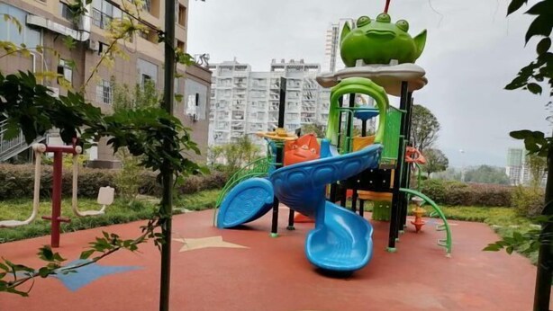 Un'area giochi con uno scivolo e strutture per arrampicarsi, immersa nel verde e circondata da edifici residenziali.