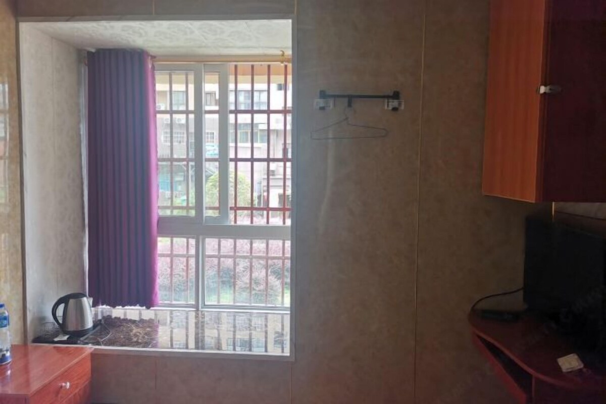 Une chambre avec une fenêtre, une bouilloire, un téléviseur et un meuble en bois.